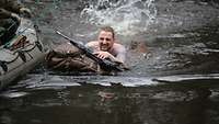 Ein Soldat schwimmt mit Rucksack und Gewehr