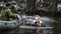 Eine Frau schwimmt mit Rucksack und Gewehr