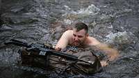 Ein Soldat schwimmt mit Waffe und Rucksack der den See