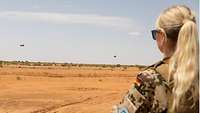 Eine Soldatin in der Wüste blickt in Richtung Horizont, wo Hubschrauber zu sehen sind 