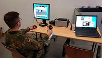 Ein Soldat sitzt mit einem Joystick in der Hand vor einem Bildschirm, daneben liegt ein Laptop.