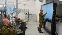 Mehrere Soldaten sitzen vor einem Whiteboard, an dem ein Soldat steht und darauf schreibt.