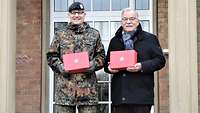 Ein älterer Mann in Zivilkleidung übergibt Geschenkpakete an einen Mann in Uniform.