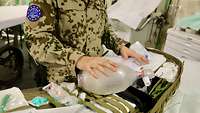 Ein Soldat steht vor einem geöffneten Sanitätsrucksack und hält ein Beatmungsgerät in der Hand