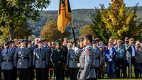 Ein Soldat trägt eine große Fahne, zahlreiche Soldaten sind angetreten.