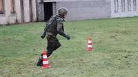 Ein Soldat mit Helm mit Schutzweste läuft um Pylonen