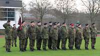 Soldaten sind in zwei Reihen auf einer Wiese vor einem Gebäude angetreten.