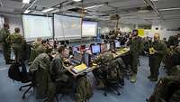 Soldaten verschiedener Nationen in einem großen Raum mit vielen Laptops, Monitoren und Lagekarten.