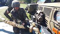Soldat im Feldanzug mit Gefechtshelm befestigt eine Kette an einem Fahrzeug.