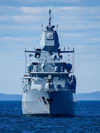 Frontal view of the frigate at sea, coastline in the background