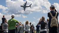 Besucher beobachten ein Transportflugzeug vom Typ A400M am Himmel