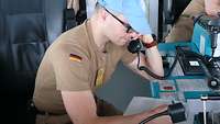 Auf der Brücke eines Schiffes sitzt ein Soldat und bedient ein Funkgerät