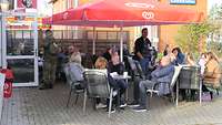 eine Gruppe Menschen sitzen lachend unter Sonnenschirmen mit einer Tasse Kaffee