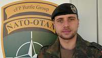 Ein Soldat steht vor dem Wappen der „Enhanced Forward Presence Battle Group Lithuania“