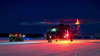 Im Schein der Positionslichter steht ein Hubschrauber auf einer verschneiten Landebahn.