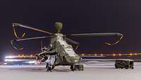 Bei Dunkelheit steht ein Kampfhubschrauber Tiger auf einer verschneiten Landebahn.