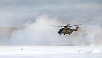 Um einen schwebenden Hubschrauber wird eine große Schneewolke aufgewirbelt.