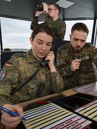 Eine Soldatin und ein Soldat sitzen im Tower eines Flugplatzes nebeneinander und arbeiten.