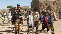 Ein Soldat läuft neben einer Gruppe Kinder durch ein malisches Dorf