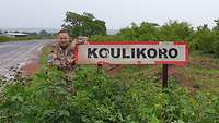 Ein Soldat steht neben dem Ortsschild von Koulikoro