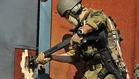 Ein Soldat hält eine schwarze Schrotflinte vom Typ Pumpgun Remington 870 an eine Tür und schießt sie auf