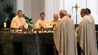 Der Weihbischof im liturgischen Gewand steht mit weiteren Geistlichen betend am Altar.