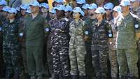 Soldaten mit hellblauen Basecups verschiedener Nationen stehen in Reihen hintereinander.