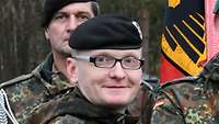 Ein Soldat mit schwarzem Barett und Brille schaut freundlich in die Kamera.