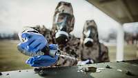 Ein Soldat in ABC-Schutzkleidung mit Kampfstoffspürpumpe an einer Flüssigkeit
