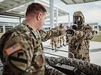 Ein amerikanischer Soldat gibt einem deutschen Soldaten in ABC-Schutzkleidung ein Autoinjektor in die Hand