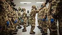 Soldaten in ABC-Schutzkleidung stehen sich gegenüber während zwei Soldaten die ABC-Masken überprüfen