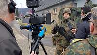 Ein Kameramann filmt und ein Journalist interviewt mit Mikrofon einen Soldaten.