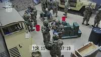 Blick auf Soldaten in ABC-Schutzkleidung zwischen Militärfahrzeuge, Fässer und Kisten in einem Raum 