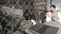 Ein Soldat sichert zahlreiche Taschen im Transportraum eines Flugzeugs mit einem Netz