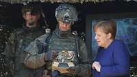 Ein Soldat hält ein Tablet in den Händen, neben ihm steht eine Zivilistin in einem blauen Blazer.