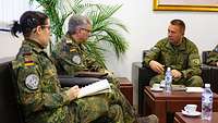 Zwei Soldaten und eine Soldatin in Uniform sitzen um einen Tisch herum und unterhalten sich