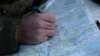 Auf einer Landkarte trägt ein Soldat seinen geplanten Weg mit einem blauen Stift ein.