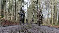 Soldaten gehen in zwei Reihen einen Waldweg entlang. Der Boden ist vom Regen matschig.