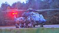 Soldaten tragen einen Verwundeten auf einem Bergetuch zu einem Hubschrauber mit roten Hecklichtern.