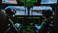 Zwei Piloten sitzen im Cockpit eines Hubschraubers. Die Messinstrumente leuchten grün. 