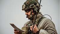 Ein Soldat mit Helm, Sprechsatz und einem Dokument in der Hand gibt einen Funkspruch durch.