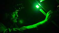 Im Dunkeln schaut ein Sanitäter unter grünem Licht auf Geräte und bedient einen Regler.