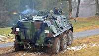 Bewaffnete Soldaten schauen aus den Luken eines Radpanzers und schießen. Mündungsfeuer ist zu sehen.