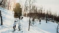 Ein Soldat mit Rucksack läuft Skiern in einer verschneiten Landschaft mit wenigen Bäumen. 