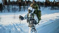 Ein Bundeswehrsoldat läuft auf Skiern mit schwerem Marschgepäck durch eine Schneelandschaft.