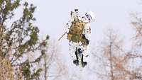Ein Soldat hängt samt Ausrüstung und Skiern an einem Windenseil eines Hubschraubers. 
