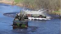 Soldaten fahren mit dem Motorboot 3 auf einem Gewässer zu einer Faltschwimmbrücke