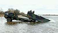 Das Brückentransportfahrzeug steht auf einer Erhöhung im Wasser und lässt das Motorboot 3 zu Wasser