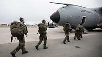 Fünf Soldaten laufen zu einem Transportflugzeug A400M um dort einzusteigen. Sie tragen ihre Ausrüstung bei sich