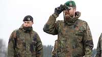 Zwei Soldaten auf einem freien Feld, einer hat ein Fernglas in der Hand, beide schauen ins Gelände.